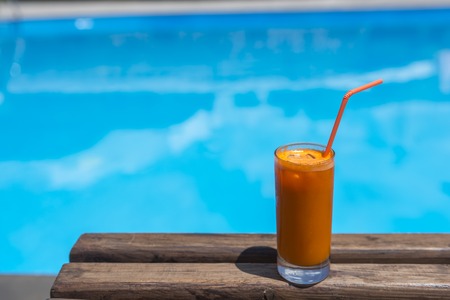 glass of fresh orange or carrot juice by the poolsideの写真素材