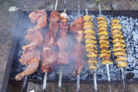 Pork and chicken meat and potatoes on skewers on the barbecue in the smokeの写真素材