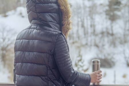 A girl in a winter jacket with coffee or tea in her hand on the balcony in winterの写真素材