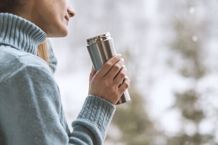 Woman in the background of a winter forest in a thermal bottle in hands