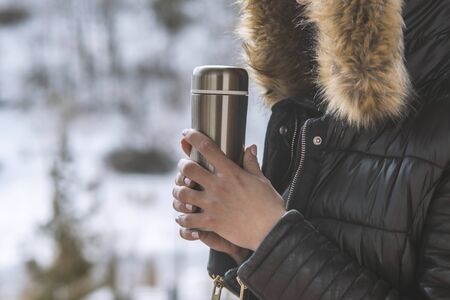 A girl in a winter jacket with coffee or tea in her hand on the balcony in winterの写真素材