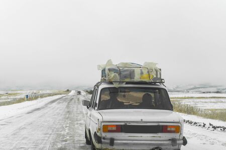 old passenger car loaded with goods on winter roadの写真素材
