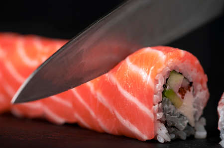 Preparing sushi at home - close up of hands cutting a Roll on a board.