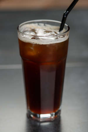 Ice coffee in a tall glass over a. Cold summer drink on a dark background with copy space