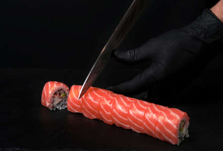Sushi roll making at home, cutting roll with avocado and salmon, home made sushi, selective focus