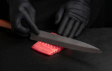 Chef cut fresh red salmon fish with sharp knife on black board. He is working on sashimi. Preparing...