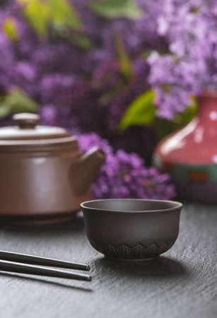 Brown ceramic asian teapot, tea cups and chopsticks on background of purple flowers. Japanese food conceptの写真素材