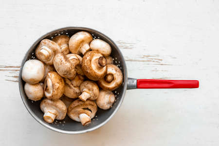 Raw mushrooms in an iron bowl on a white wooden backgroundの写真素材