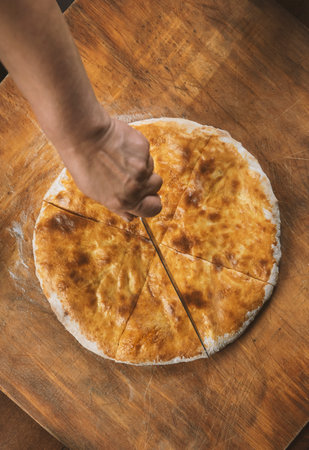 Person cutting homemade cheese pie on wooden background. Bulgarian banitsa, Georgian khachapuri,...