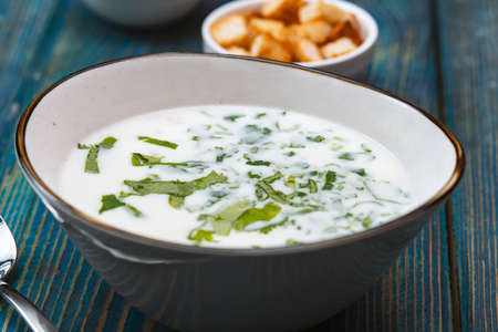 yogurt soup with herbs and crackers on a blue wooden tableの写真素材
