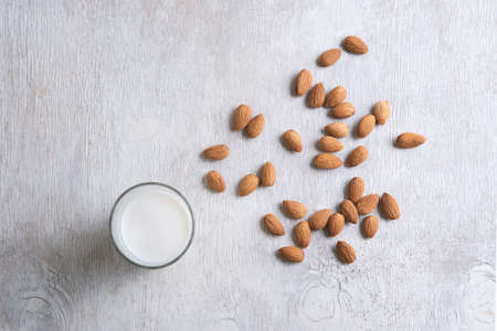 Close up top view of healthy almond milk in drinking glass and almond seed on white wooden table...