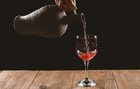 girl hands pouring red wine into a glass from a clay bottle on a black backgroundの写真素材