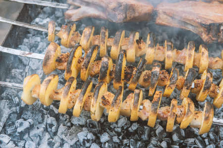 Pork and chicken meat and potatoes on skewers on the barbecue in the smokeの写真素材
