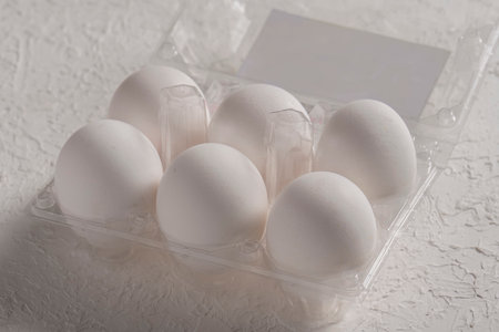 Open box with six whole white eggs on white background. Fresh organic chicken eggs in plastic pack or egg containerの写真素材