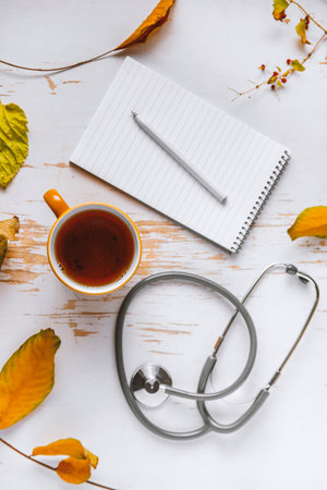 Top view of hot coffee served on shabby table with stethoscope and scattered yellow leaves