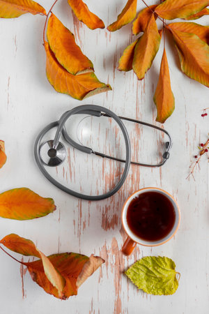 Top view of hot coffee served on shabby table with stethoscope and scattered yellow leavesの写真素材