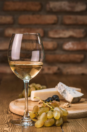 still life with white wine and cheese on a wooden tableの写真素材