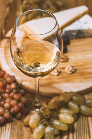 still life with white wine and cheese on a wooden tableの写真素材