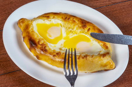 Man eating adjar Khachapuri. Georgian national pie khachapuri with egg and cheese in the white plate on wooden background.の写真素材