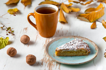 Baked pie served with hot tea on table with dried leaves and walnuts .autumn composition