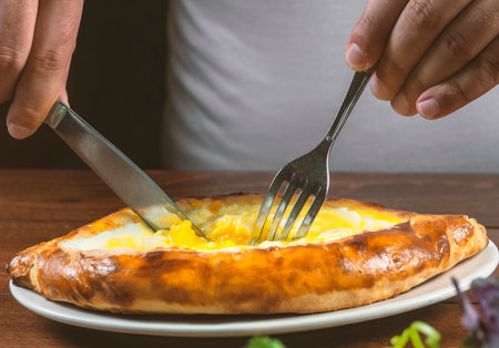 Man eating adjar Khachapuri. Georgian national pie khachapuri with egg and cheese in the white plate on wooden background.の写真素材