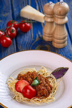 spaghetti bolognese pasta in a white plate, salt, pepper, cheese and tomatoes on blue wooden backgroundの写真素材