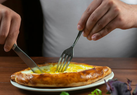 Man eating adjar Khachapuri. Georgian national pie khachapuri with egg and cheese in the white plate on wooden background.の写真素材