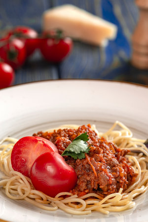 spaghetti bolognese pasta in a white plate, salt, pepper, cheese and tomatoes on blue wooden backgroundの写真素材