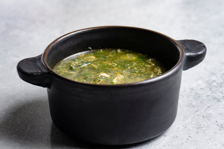 Soup with green sorrel in black ceramic pot on gray backgroundの写真素材