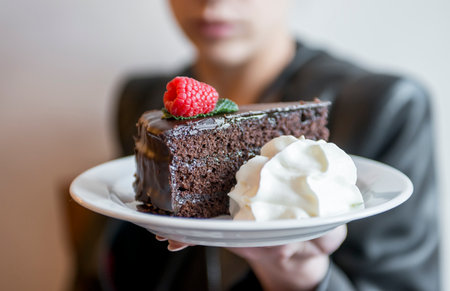 Woman showing chocolate cake with whipped cream, defocused backgroudの写真素材