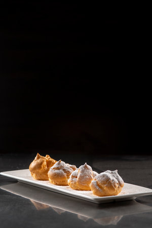 Eclairs with icing sugar on black background. Decorating profiteroles with powdered sugar.