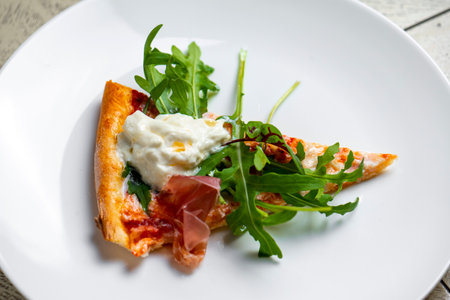 piece of pizza with smoked salmon and arugula on a white plate