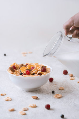 bowl of corn granola with milk, fresh raspberries, blueberries .and a glass on white wooden board for healthy breakfast,の写真素材