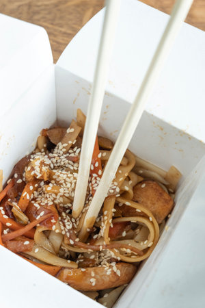 chinese noodle with chopsticks in take away box on wooden tableの写真素材
