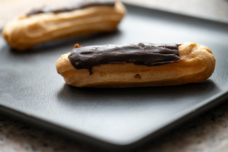 Chocolate eclairs on a black plate.