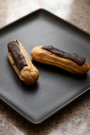 Chocolate eclairs on a black plate.