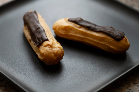 Chocolate eclairs on a black plate.