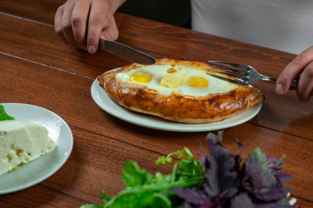 Man eating adjar Khachapuri. Georgian national pie khachapuri with egg and cheese in the white plate on wooden background.の写真素材