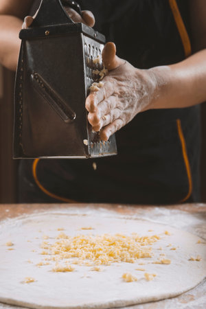 Chef grating cheese into dough in restaurant kitchen.の写真素材