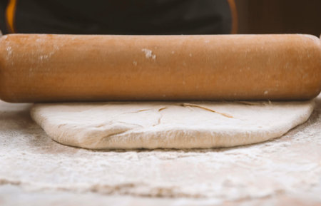 Rolling the dough with the rolling pin on the table. Hands close-up. Cooking pasta, bread, food...