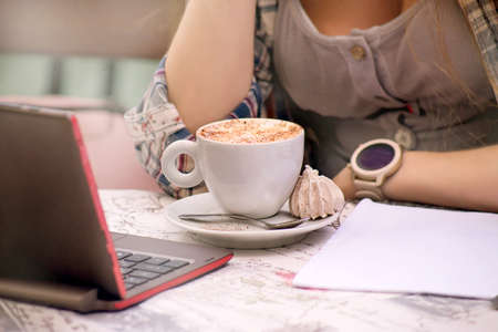a young girl works on a computer, in a cafe, at lunchtime, a cup of coffee close-upの写真素材