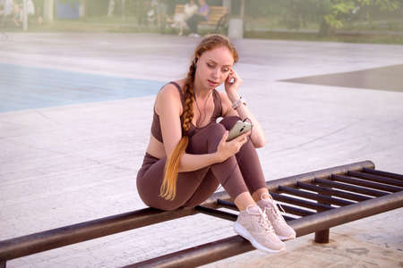 girl chooses music on the phone for doing sports exercises outdoors, healthy lifestyle concept