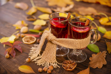 Two glasses of hot wine wrapped in one warm scarf on wooden table background, copy space. Autumn, autumn leaves. Seasonal drink, relaxing Sunday and the concept of care, love, warmの写真素材
