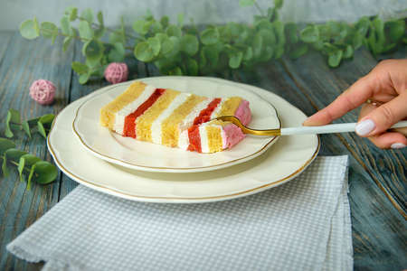 Female hand cutting vanilla homemade birthday cake with whipped cream, on wooden table, side view,...