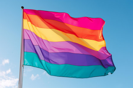 Rainbow flag waving in the wind against a blue sky background.の素材