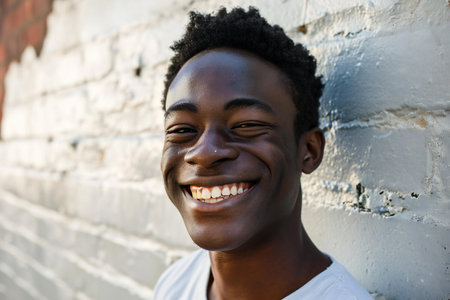 Close up portrait of a smiling young african american man against brick wallの素材