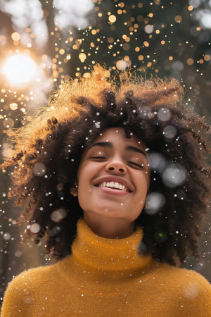 Beautiful african american girl with afro hairstyle in yellow sweater smiling and looking at camera in winter parkの素材