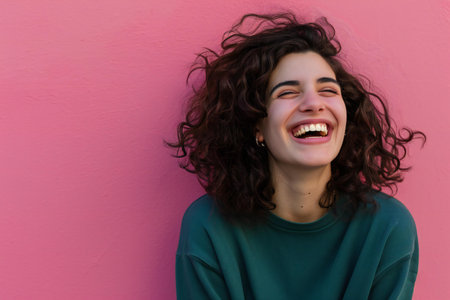 Portrait of a young woman with curly hair laughing against pink backgroundの素材