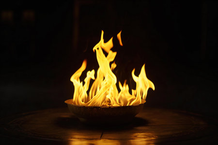Burning fire in a bowl on wooden table with dark background.の素材