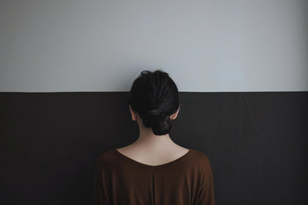 Back view of a young woman with black hair standing in front of a wallの素材
